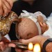Baby bliver døbt under en barnedåb med vand hældt over hovedet.