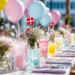 Farverigt pyntet bord til nonfirmation med blomster, balloner og danske flag i lyserøde og blå nuancer.