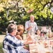 Festtale ved havefest, hvor gæster samles omkring bordet til hyggeligt samvær.