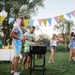 Sommerfest i haven med grill, farverig pynt og gæster, der hygger sig udendørs.